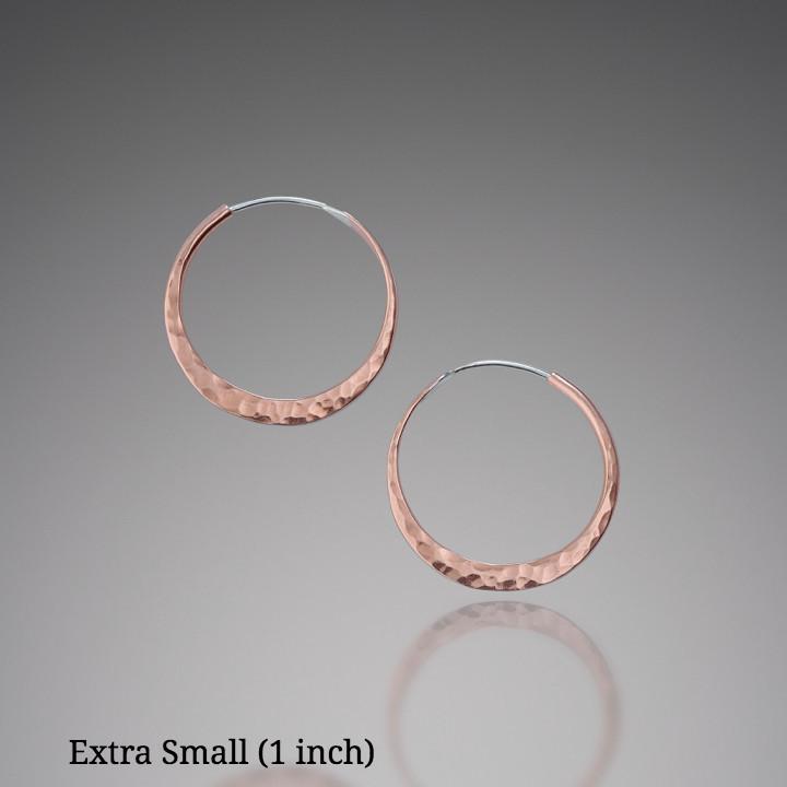 Artisanal hammered copper hoop earrings by Mostly Sweet Jewelry in extra small size (1 inch diameter). These minimalist circular earrings feature a textured, hand-forged finish that creates organic light-reflecting patterns across the warm copper metal. The sleek, lightweight design offers versatile everyday wear. Perfect for bohemian, rustic, or contemporary styling. Ethically crafted metalwork jewelry suitable for sensitive ears.