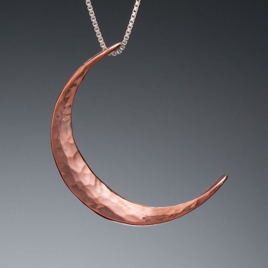 Handcrafted copper crescent moon pendant by Mostly Sweet Jewelry on silver box chain. Features hammered texture with warm coppery tone against gray background. The elegant curved design catches light along its textured surface, creating subtle dimension. Perfect celestial accessory for nature-inspired or bohemian styling.