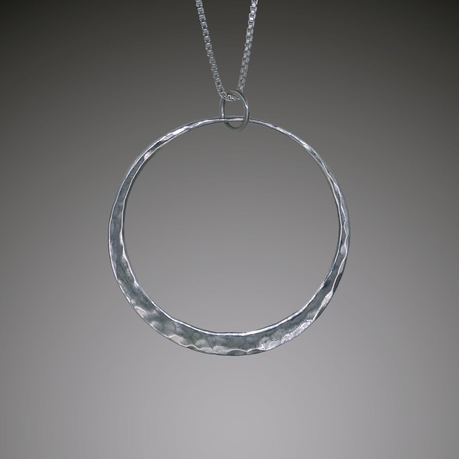 Handcrafted sterling silver Eclipse pendant by Mostly Sweet Jewelry. Features a minimalist circular design with hammered texture that catches light. The open circle symbolizes celestial phenomena, suspended from a delicate silver box chain against gray background. Simple yet elegant statement piece for astronomy enthusiasts and minimalist jewelry lovers.